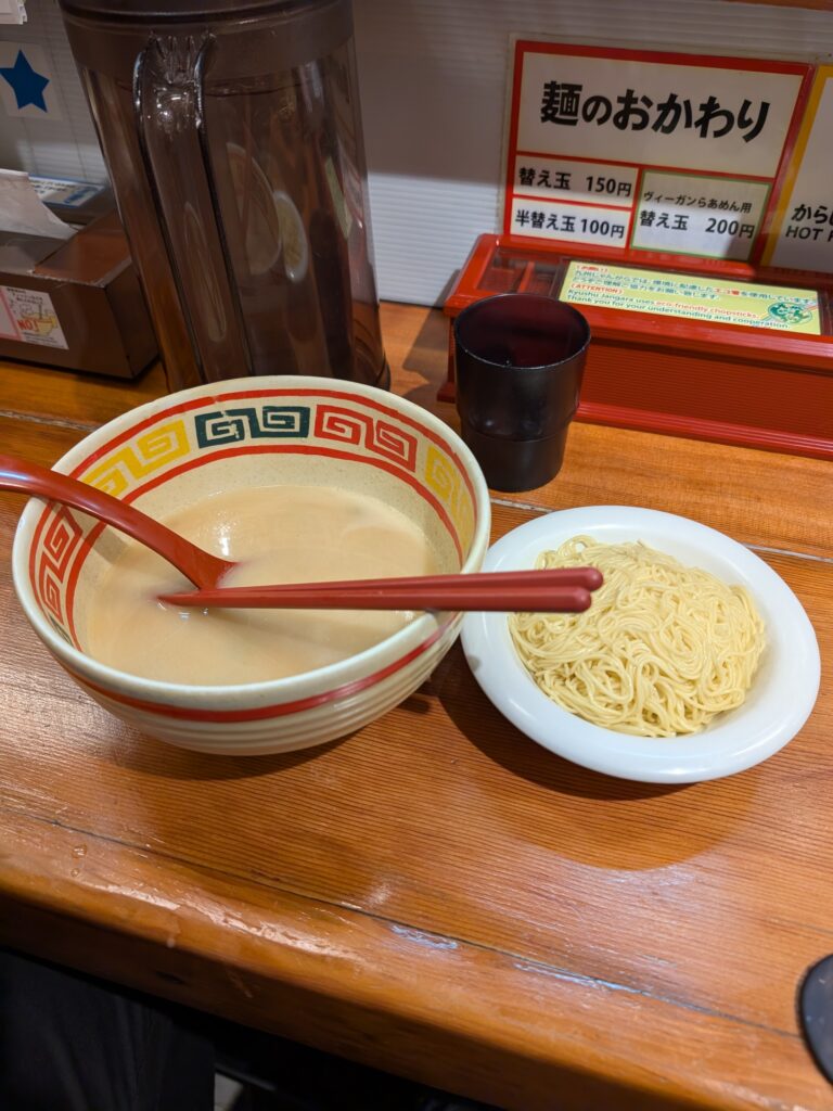 a refill of noodles next to a bowl of broth